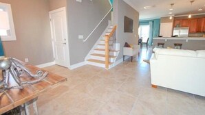 A spacious living area with a staircase, a white sofa, and a kitchen in the background. - South Beach Cottages - 2716 Apartment 3 (Myrtle Beach)