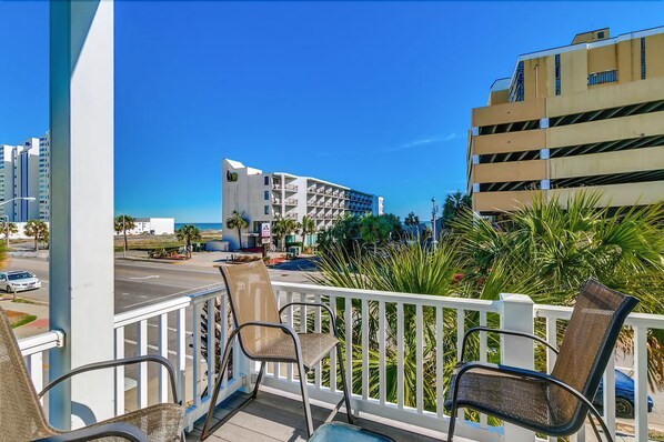 A balcony with chairs, a view of a building with multiple floors, and palm trees. - South Beach Cottages - 2613 Apartment 4 (Myrtle Beach)