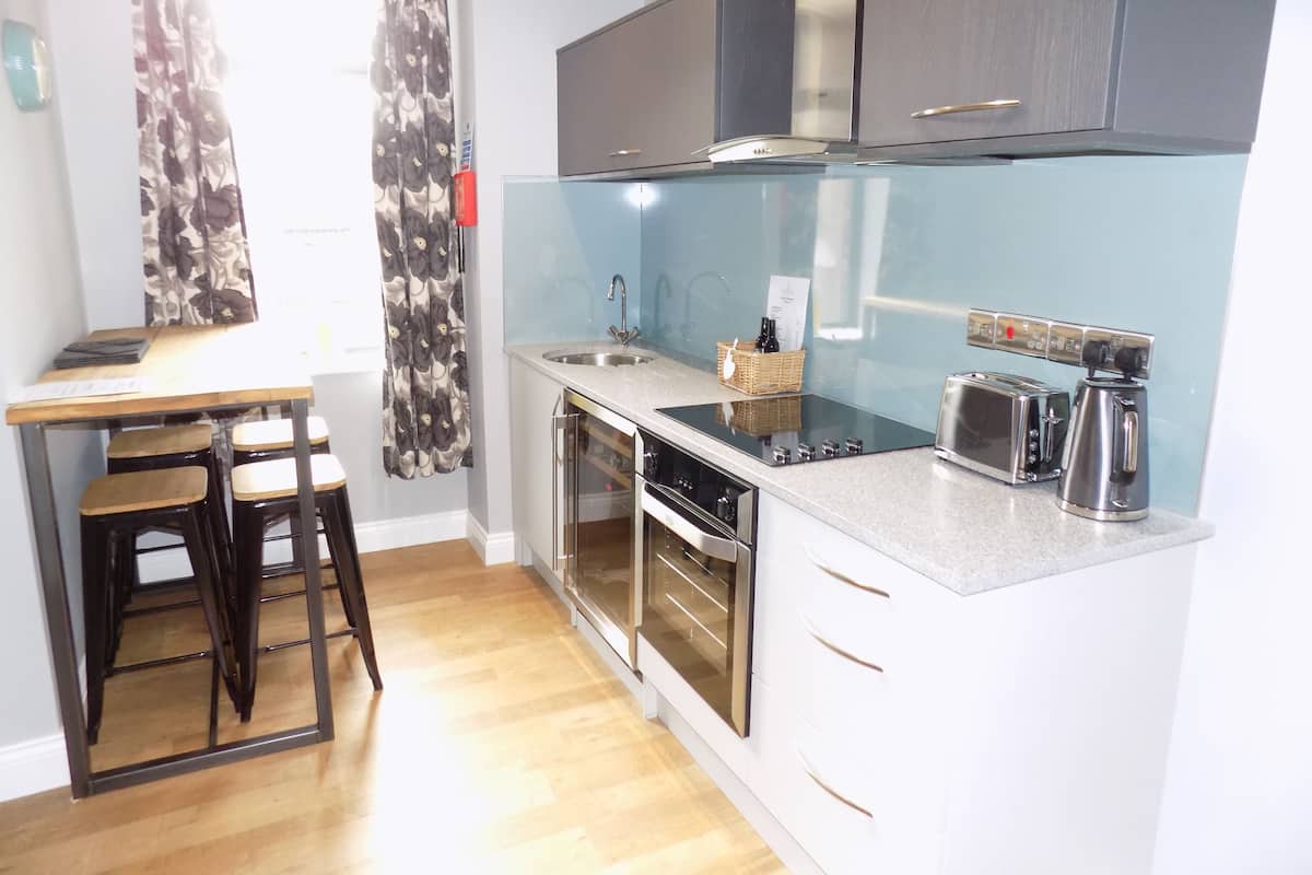 A compact kitchen with a stove, oven, and toaster. There is a small dining area with stools and a table.