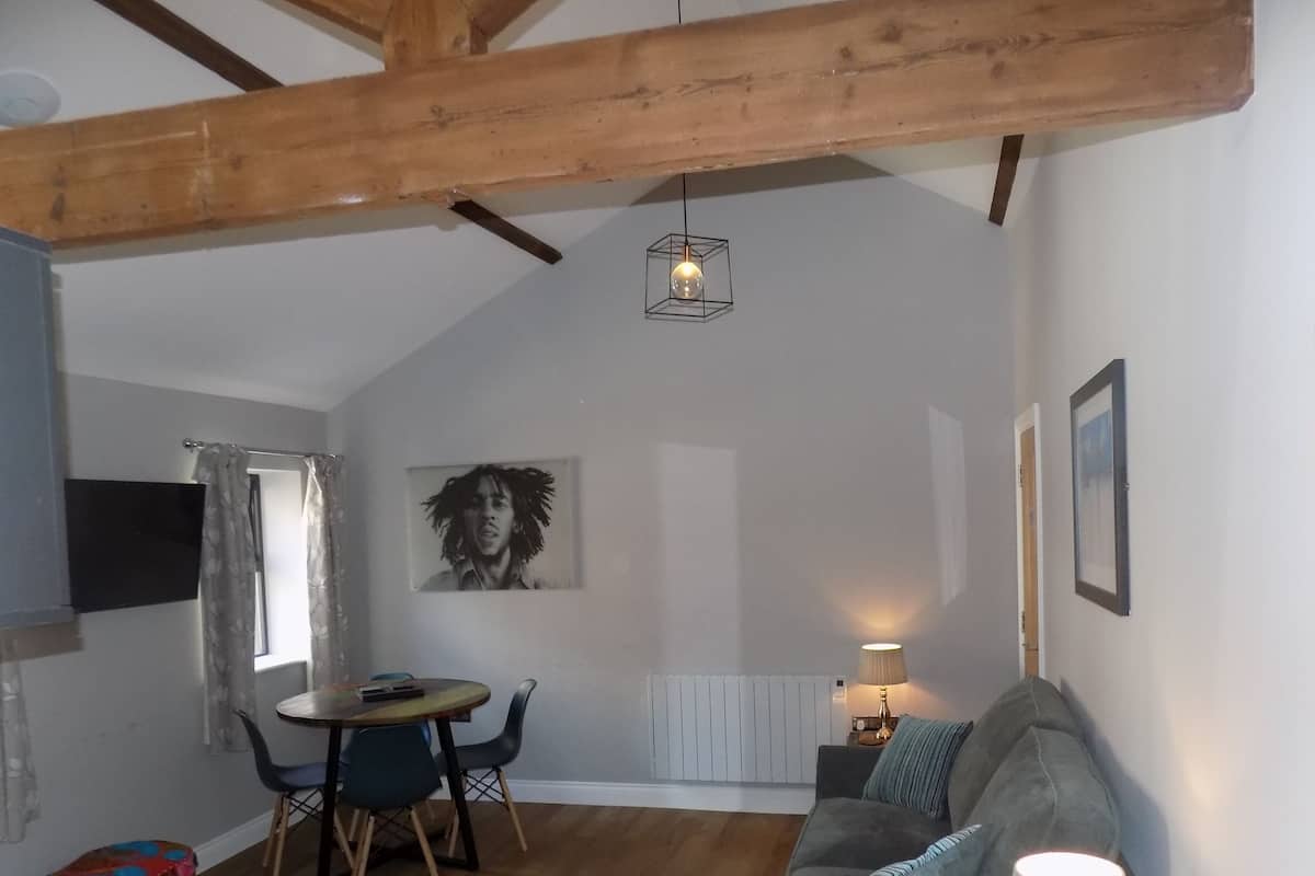A cozy living room with a wooden ceiling, a dining table with chairs, a sofa, and a lamp.