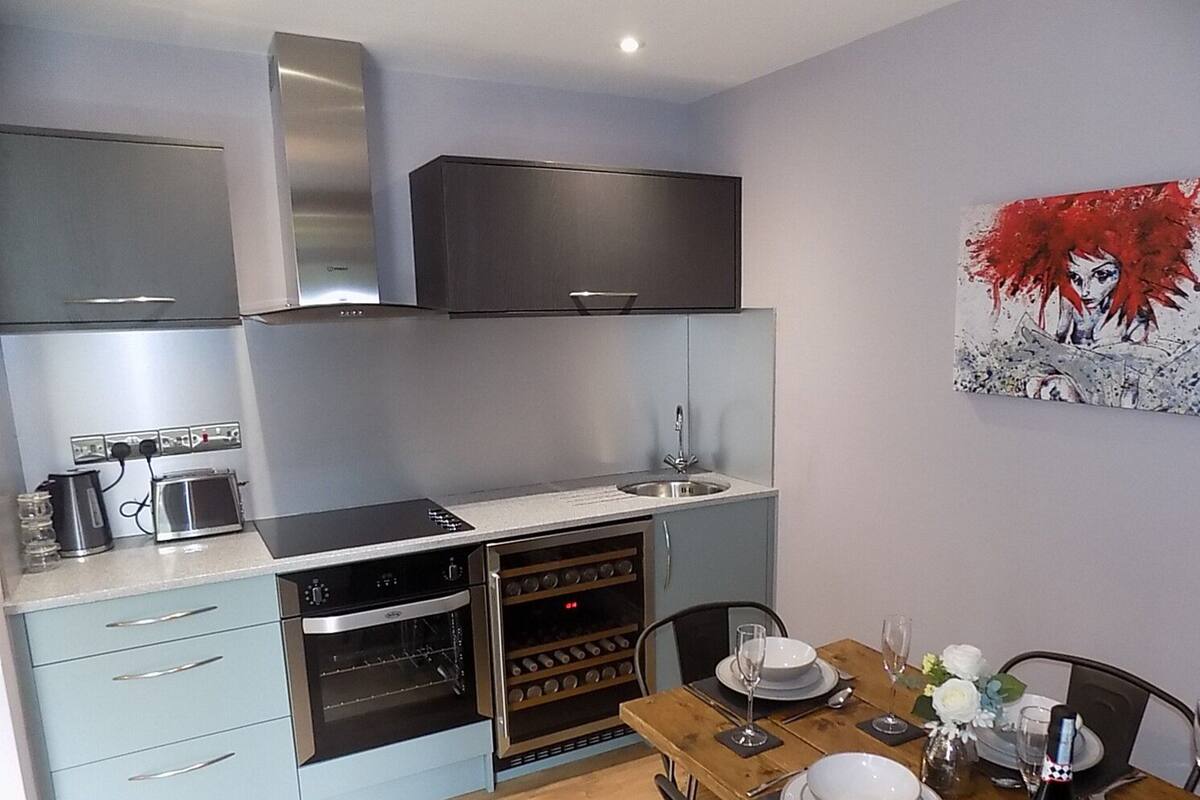 A compact kitchen with a built-in oven, a microwave, and a sink. There is a dining table with chairs and a vase of flowers.
