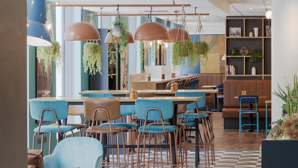 Ein modernes Café mit blauen Stühlen, Holztischen, hängenden Pflanzen und einem Schachbrettmuster auf dem Boden.