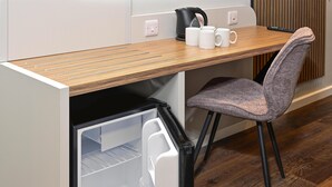 Eine kleine Küchenzeile mit integriertem Kühlschrank, einer Holz Arbeitsplatte und einem grauen Stuhl.