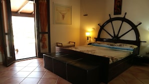 A bedroom with a bed, a wooden headboard, a nightstand, a wall-mounted lamp, and a door leading to an outdoor area. - Aurelio Rapillo (Latina)