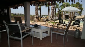 An outdoor patio with a table and chairs, a striped umbrella, and a view of a pool and palm trees. - Aurelio Rapillo (Latina)