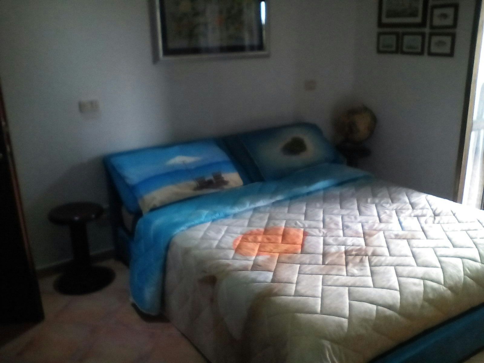 A bedroom with a bed, a small round table, and a wall with framed pictures.