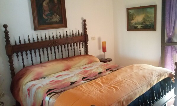 A bedroom with a wooden headboard, a floral bedspread, and two framed artworks on the wall. - Aurelio Rapillo (Latina)