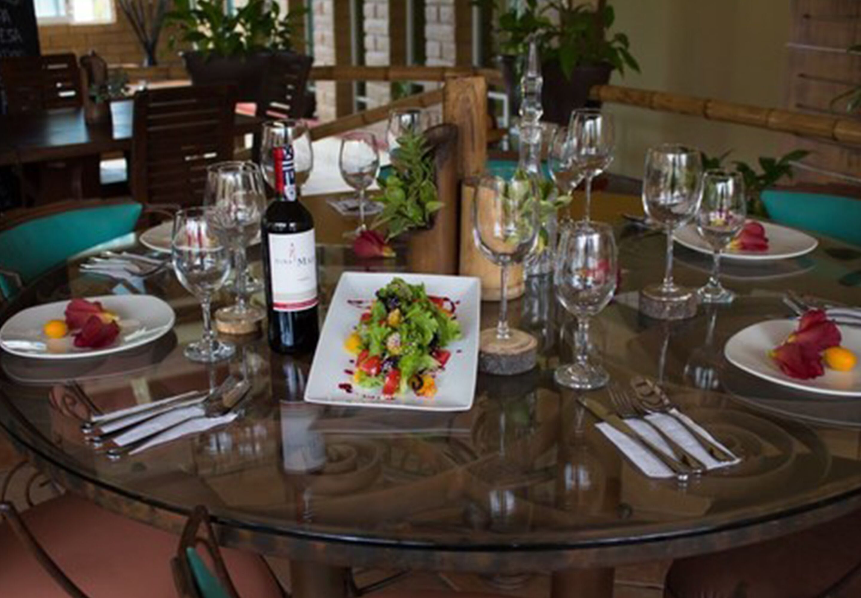 A dining table set with plates, cutlery, wine glasses, and a bottle of wine.