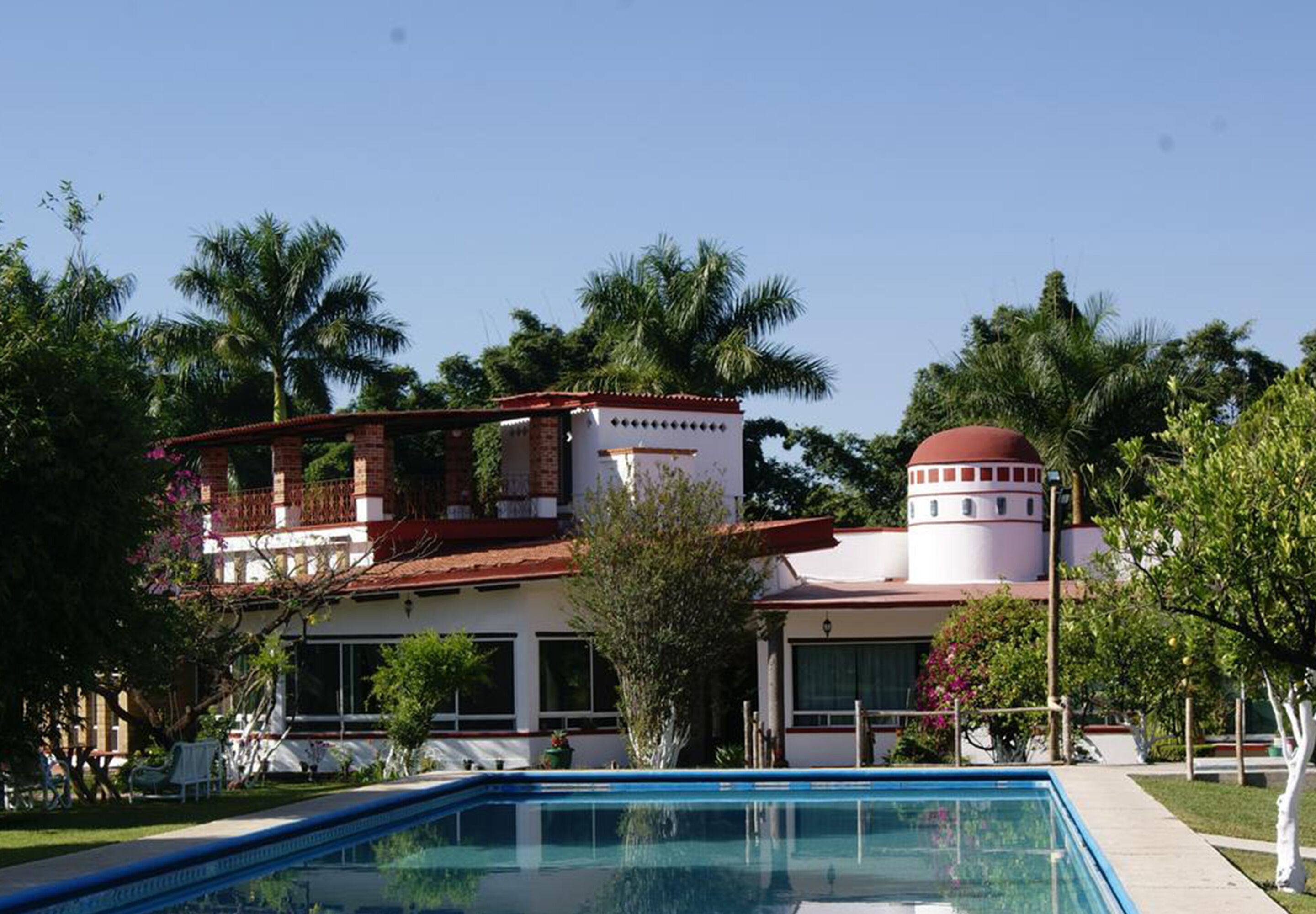 A hotel with a swimming pool, a red-roofed tower, and palm trees in the background.