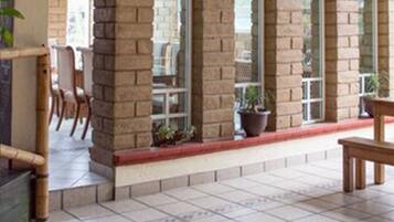 A spacious indoor area with tiled flooring, brick pillars, and large windows.