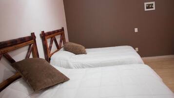 Ein Zimmer mit zwei Betten, Holz-Kopfteilen, weißer Bettwäsche und einer braunen Wand.