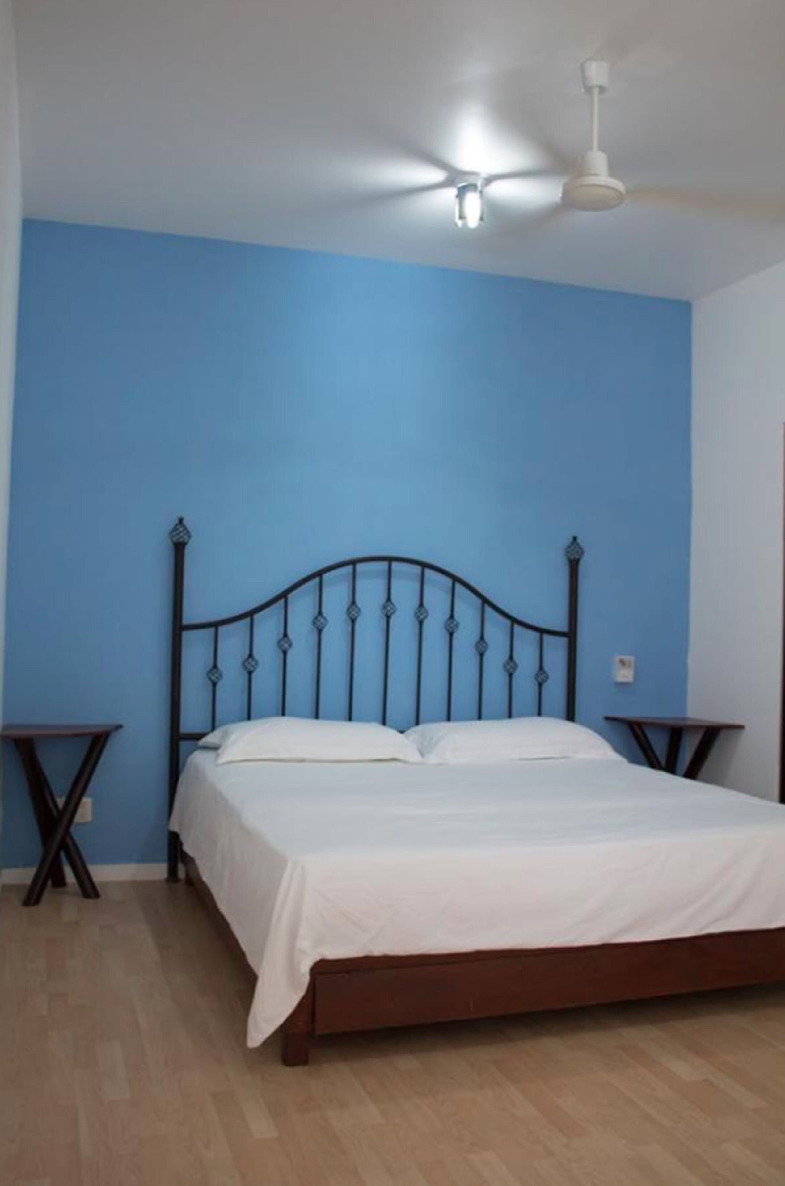 Un dormitorio con cama, ventilador de techo y dos mesitas de noche.