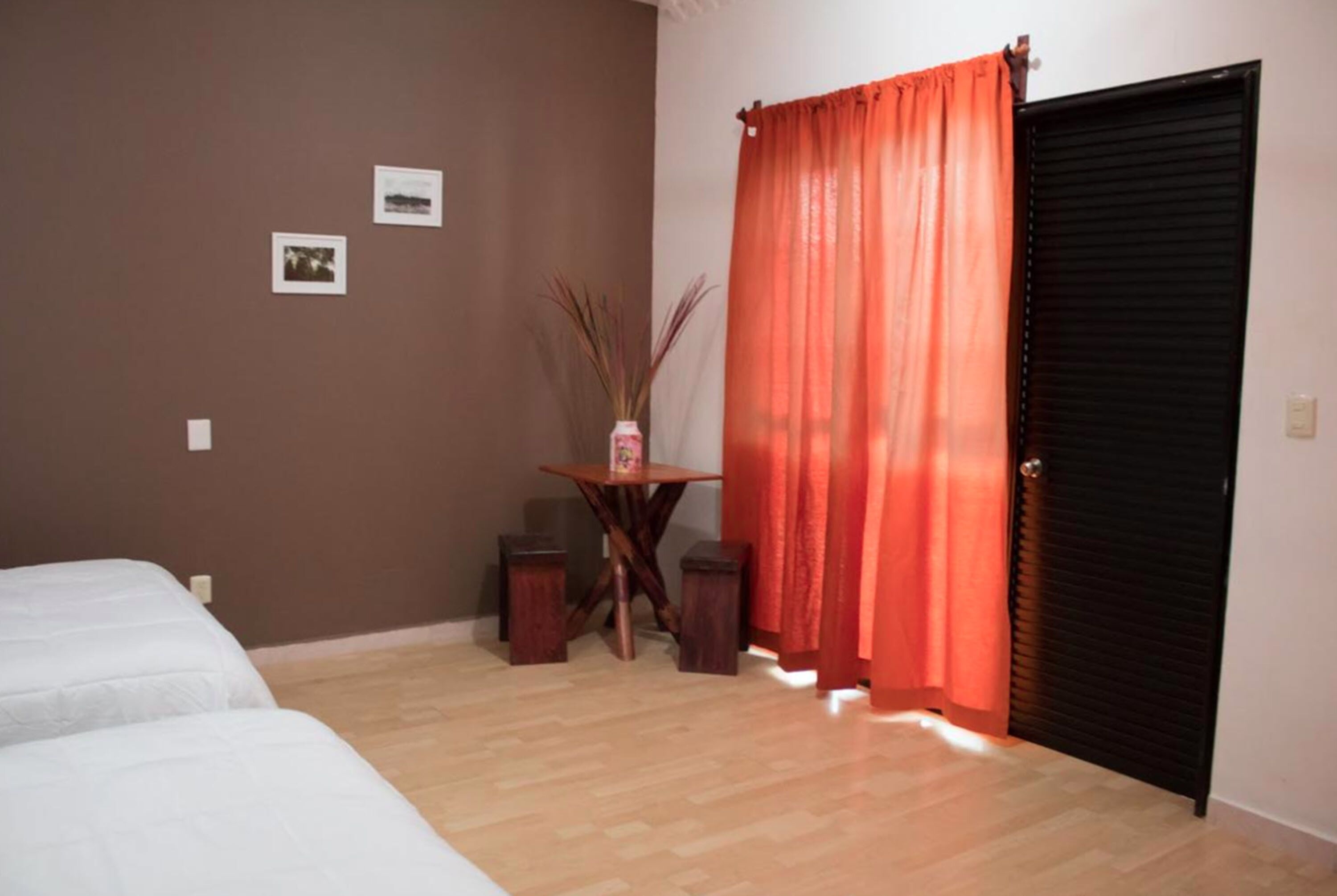 A room with two beds, a small table with a vase, and a door with a red curtain.