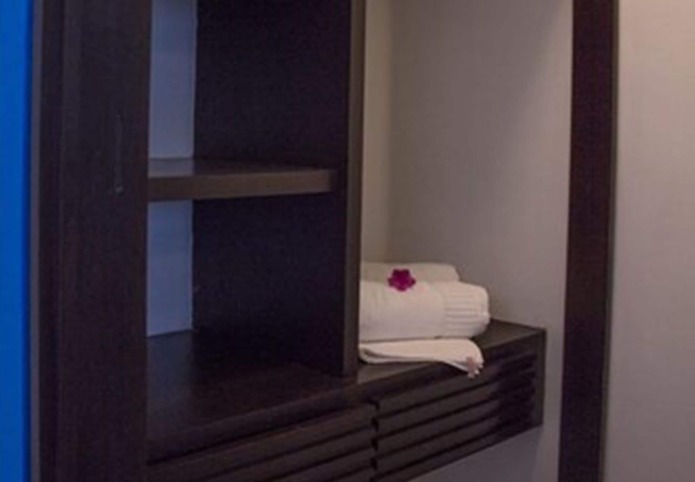 A dark wooden shelf with folded white towels and a purple flower.
