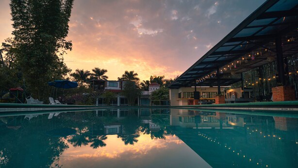 A swimming pool reflecting a sunset with buildings and palm trees in the background. - Hotel Quinta Moctezuma (Yautepec)