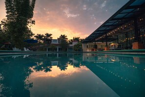 A swimming pool reflecting a sunset with buildings and palm trees in the background. - Hotel Quinta Moctezuma (Yautepec)