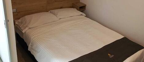 A small, single-bed room with a wooden headboard, a bedside table, and a black and white bedspread.