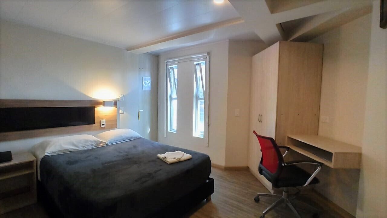 Une chambre d’hôtel avec un lit, un bureau, une chaise et une armoire.