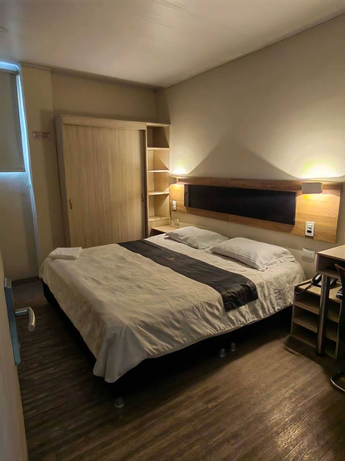 A bedroom with a bed, a wooden wardrobe, a desk, and a chair.