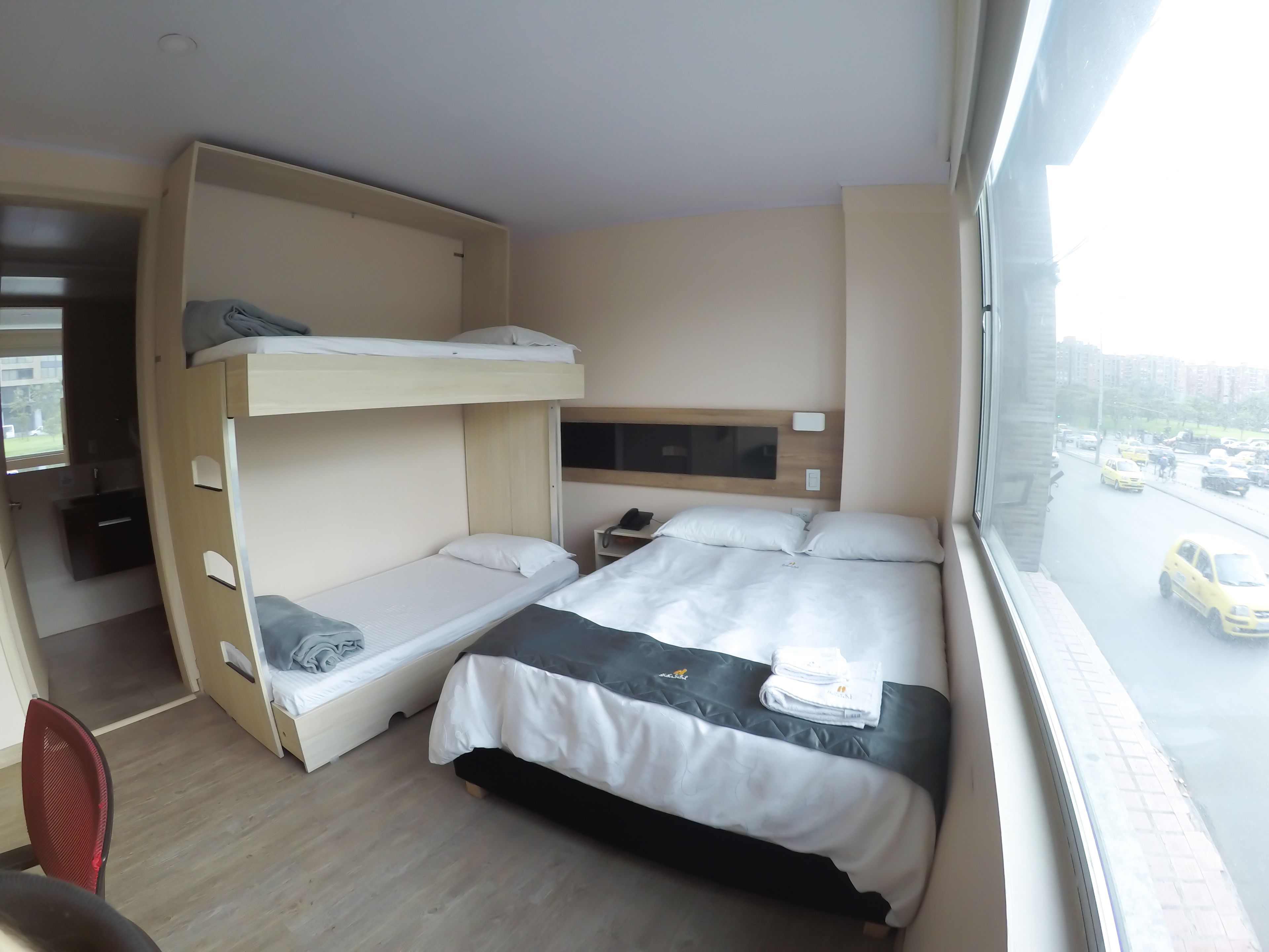 A hotel room with bunk beds, a desk, a chair, and a window with a city view.
