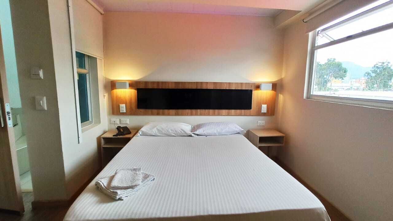 Habitación de hotel con una cama grande, mesitas de noche, televisor montado y ventana con vistas.