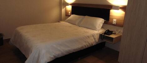 A single bed with a wooden headboard, bedside lamps, and a phone on the nightstand.