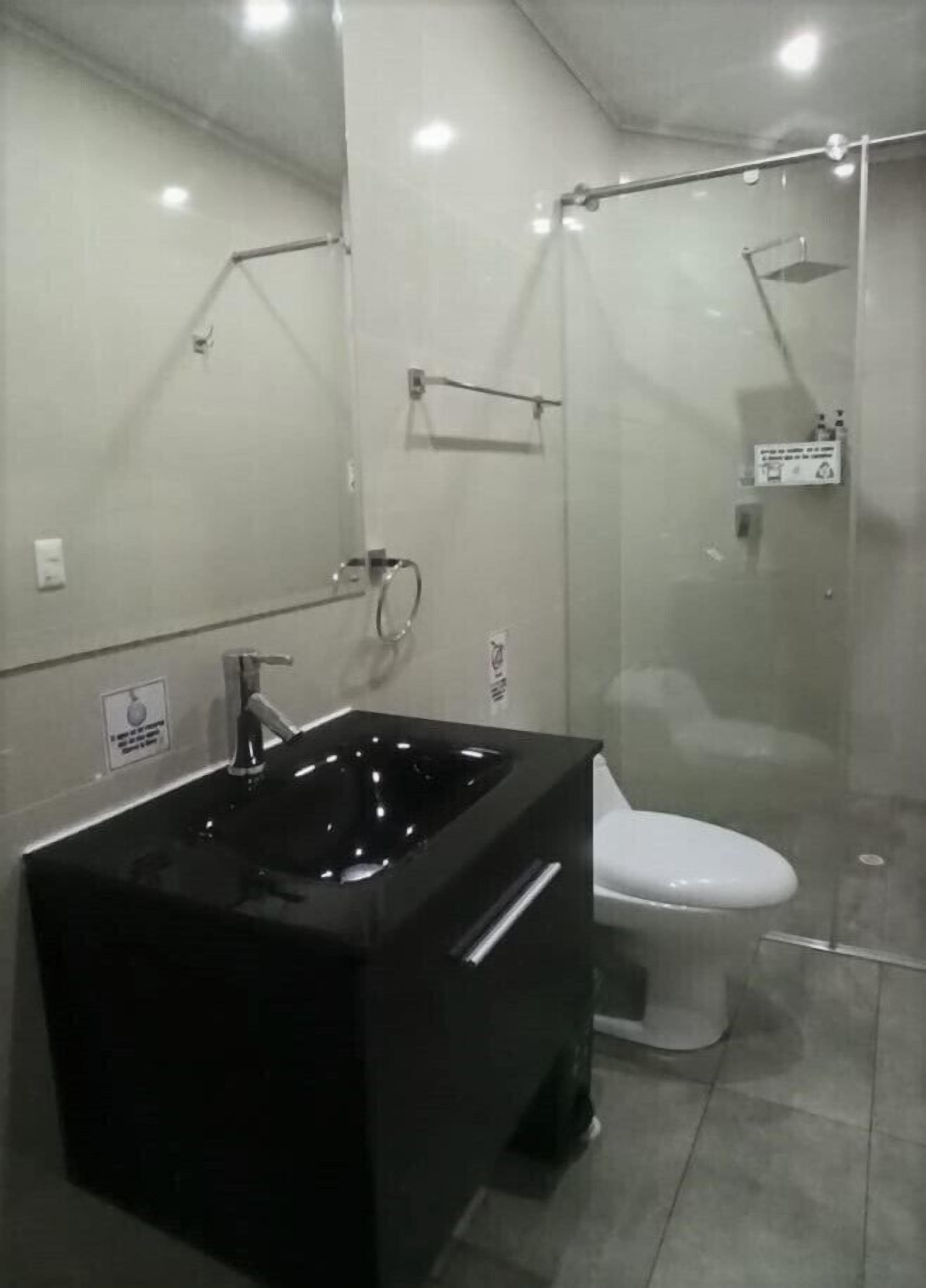 Une salle de bain moderne avec une baignoire noire, des toilettes blanches et une douche séparée par des parois en verre.