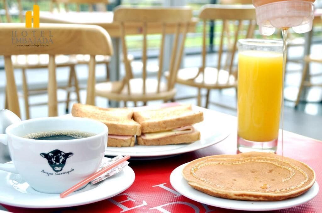 A breakfast setting with a cup of coffee, sandwiches, a glass of orange juice, and a pancake on a table.
