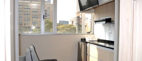 A compact kitchen with a built-in TV, a small refrigerator, and a window offering a city view.
