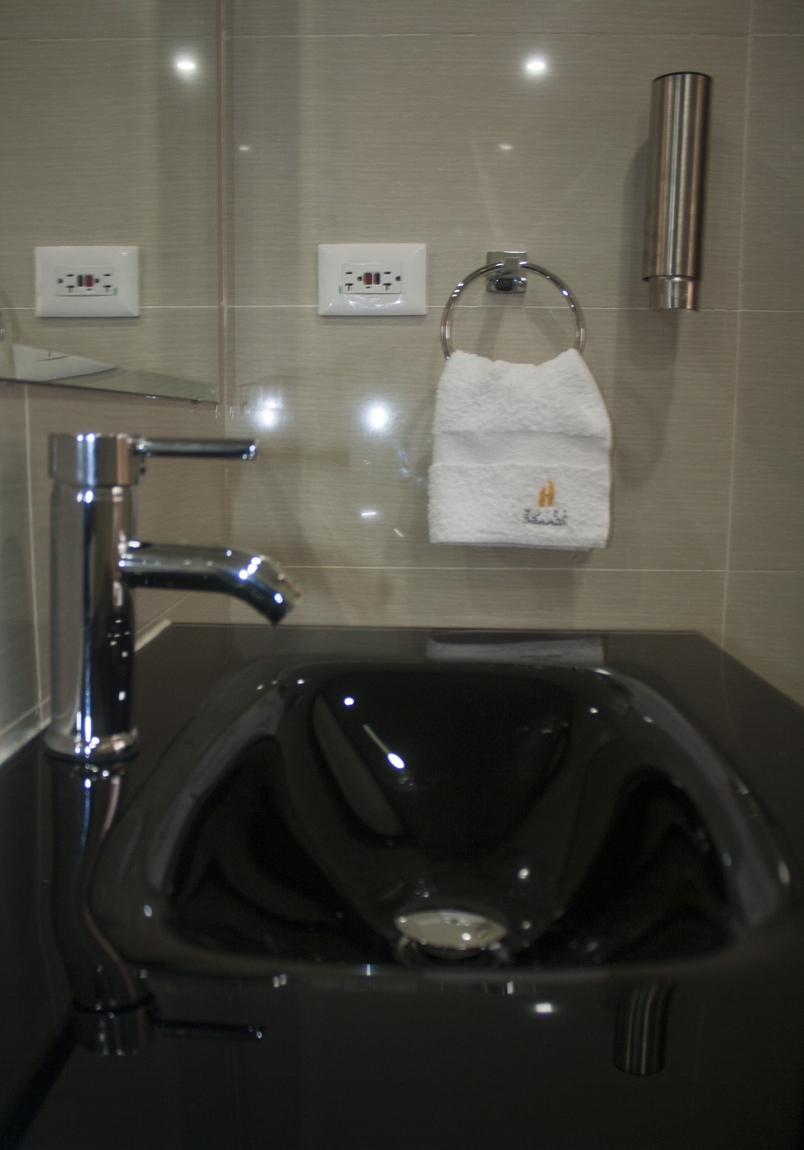Un baño moderno con un lavabo negro, grifo cromado y un tocadereje con una toalla blanca.