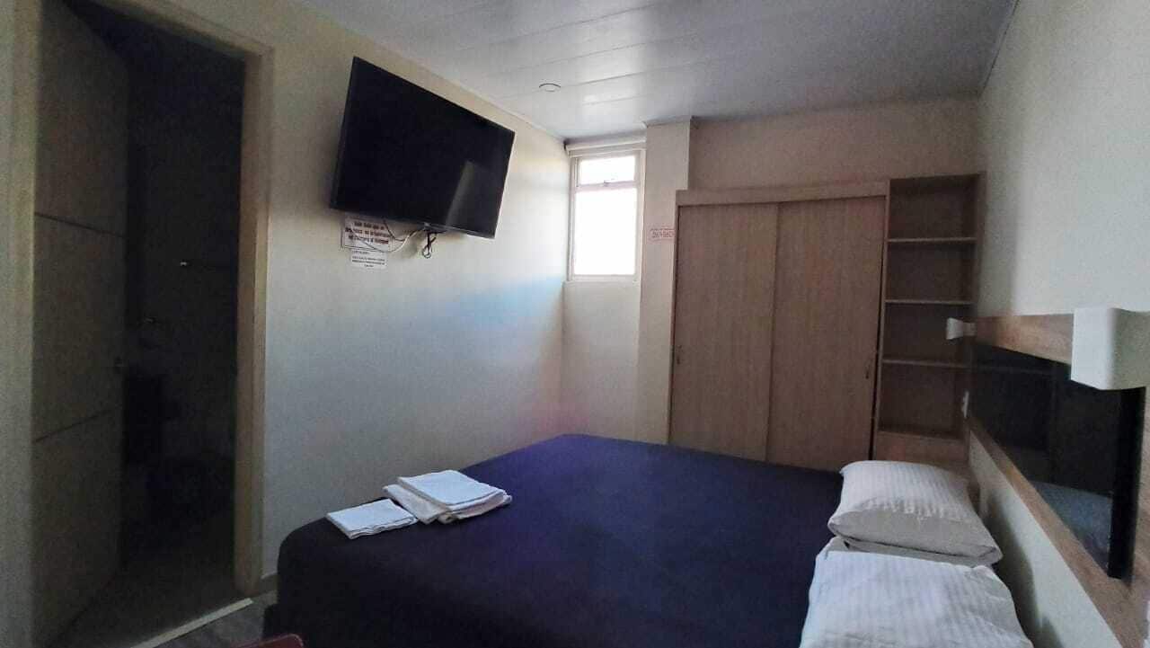 A bedroom with a bed, a TV mounted on the wall, a window, and a wardrobe.