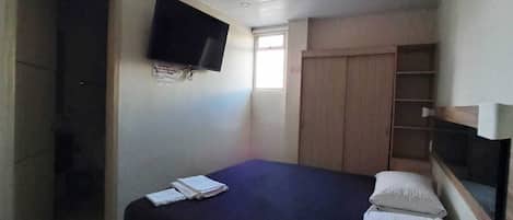 Une chambre à coucher avec un lit, un téléviseur fixé au mur, une fenêtre et une armoire.