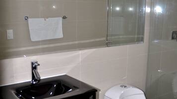 Un baño con lavamanos negro, inodoro blanco y cabina de ducha con mampara de vidrio.