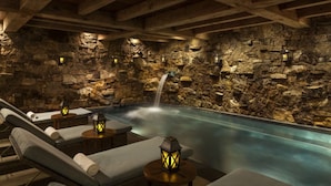 Un espace spa agrémenté d’un mur en pierre, d’un bain à remous et de chaises longues.