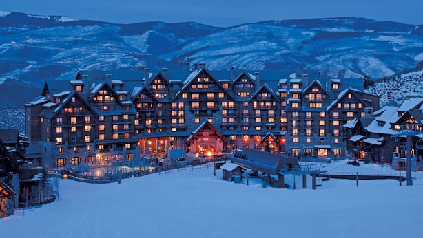 Un grand bâtiment de plusieurs étages, de style chalet, avec une façade symétrique, de nombreuses fenêtres et une entrée centrale surmontée d’une enseigne lumineuse.