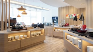 A modern kitchen with wooden cabinets, a central island with bowls and plates, pendant lighting, and a colorful abstract painting on the wall.