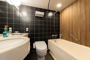 Une salle de bain moderne avec des murs recouverts de carreaux noirs, un mur en panneaux de bois, une baignoire blanche, des toilettes et un lavabo équipé d’un distributeur de savon.