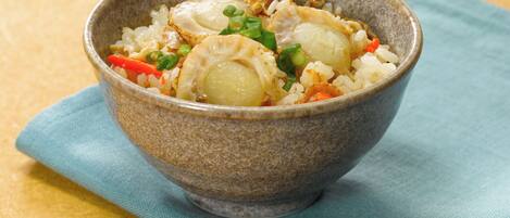 A bowl of rice with vegetables and possibly seafood, placed on a blue napkin on a textured yellow surface.