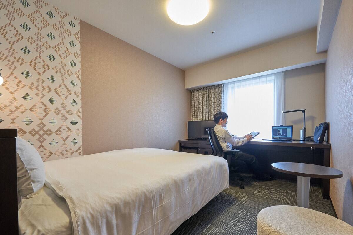 Een hotelkamer met een bed, een bureau met een laptop, een stoel en een klein tafeltje.