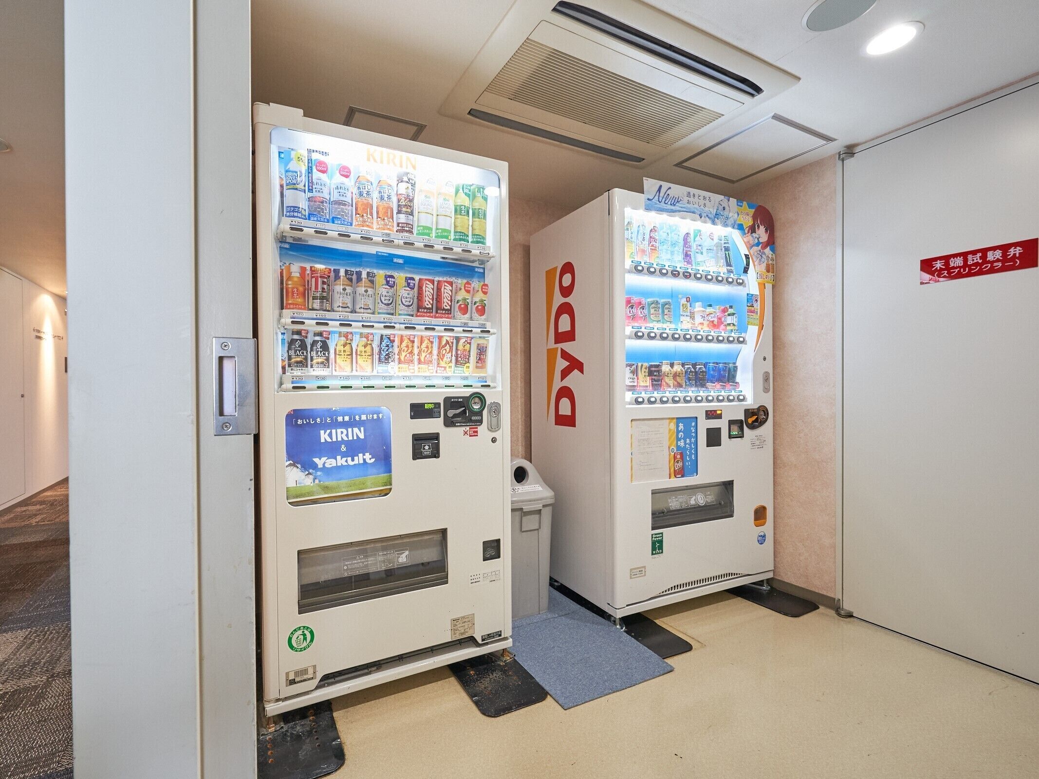 Two vending machines labeled 'DYDO' in a hallway with a carpeted floor and a door in the background.