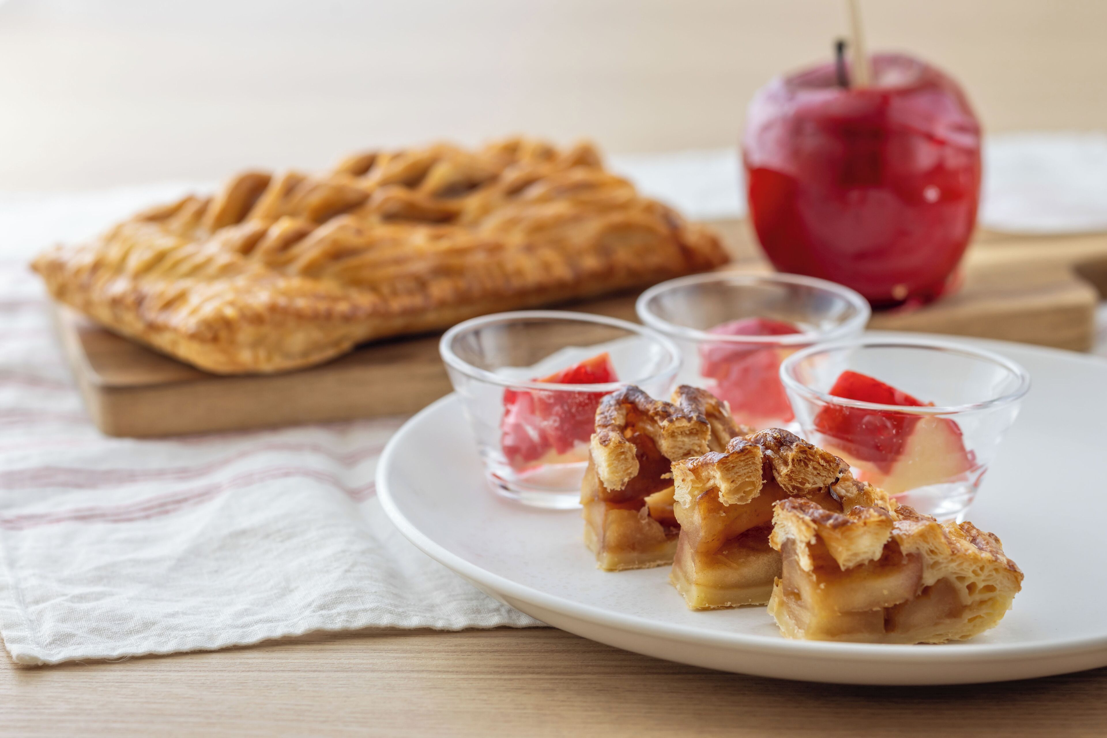 A plate with a pie, a whole apple, and two small bowls with a red substance.