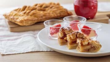 A plate with a pie, a whole apple, and two small bowls with a red substance.