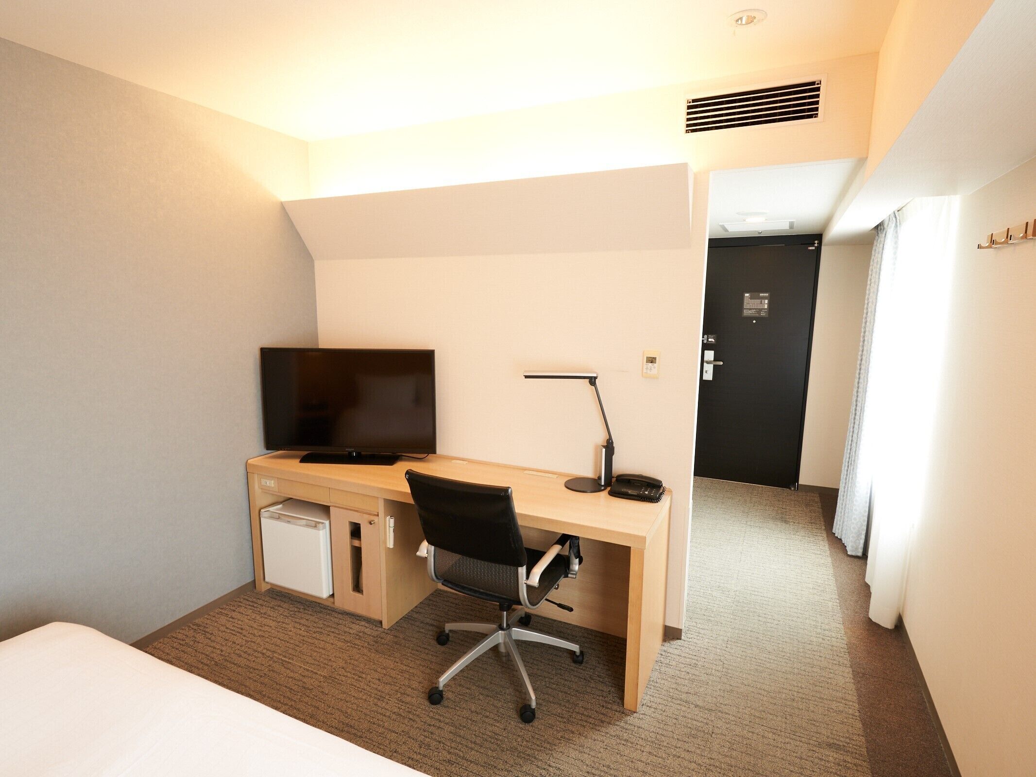 A hotel room with a bed, a desk with a computer, a TV, and a chair.