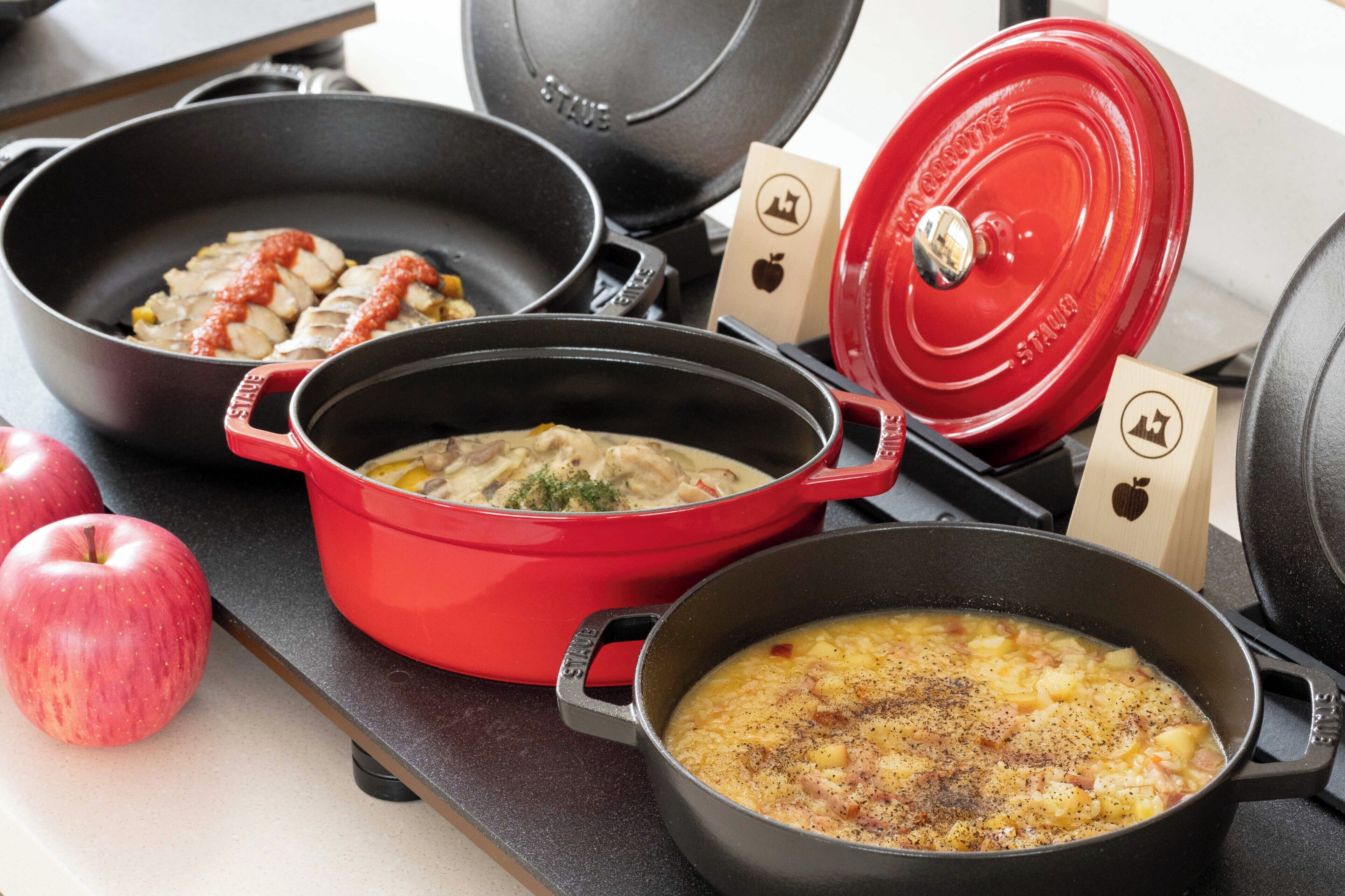 Una cocina con varias ollas y sartenes, incluyendo una olla roja y una sartén negra.