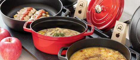 Una cocina con varias ollas y sartenes, incluyendo una olla roja y una sartén negra.