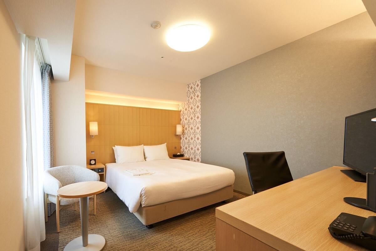 Een hotelkamer met een bed, een bureau met telefoon, een stoel, een klein tafeltje en een televisie.