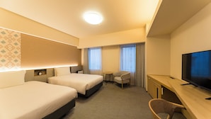 A hotel room with two beds, a desk, a TV, and a small table.