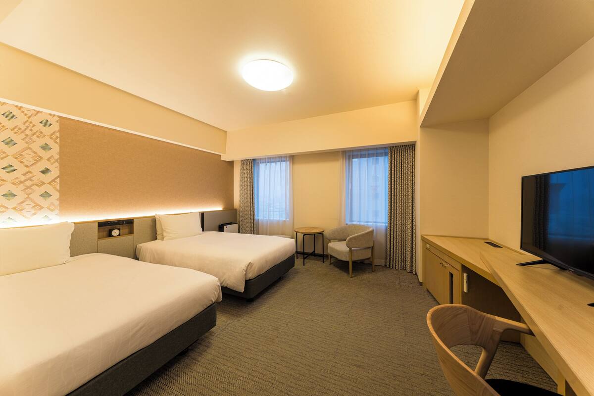 Een hotelkamer met twee bedden, een bureau, een televisie en een klein tafeltje.