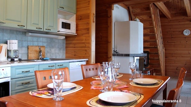 A wooden cabin interior with a dining table set for four, light blue cabinets, a white microwave, and a refrigerator. - Nuppulanranta cottage by lake (Jamsa)