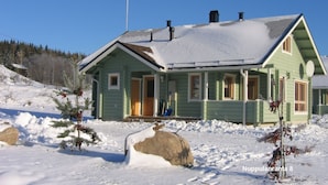 A green wooden house with a porch, surrounded by snow and trees. - Nuppulanranta cottage by lake (Jamsa)